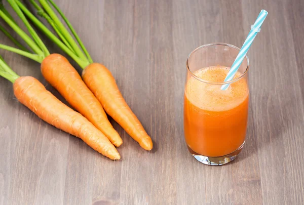 Healthy carrot smoothie in a glass and raw carrots on a wooden background