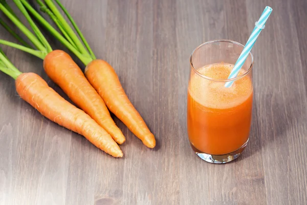 Healthy carrot smoothie in a glass and raw carrots on a wooden background