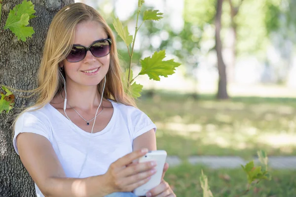 A blonde woman in a park and surfing in the net with her smartphone