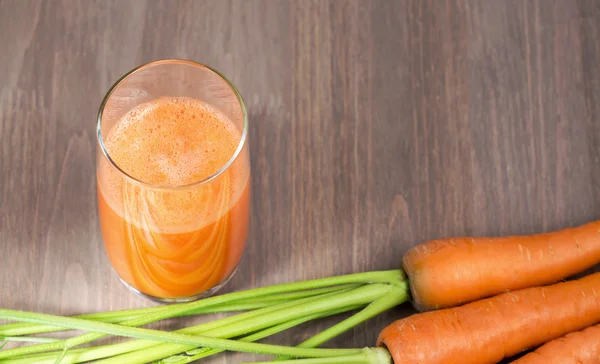 Healthy carrot smoothie in a glass with raw carrots on a wooden background