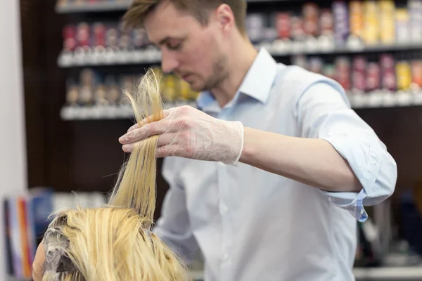 A hairdresser bleaching hair for a blonde female client