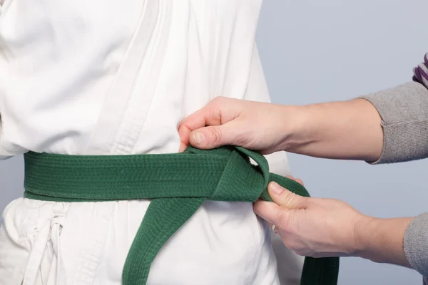 Hands of a parent who helps a child to tie a green belt