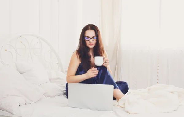 Young woman reads from tablet pc in bed, high key
