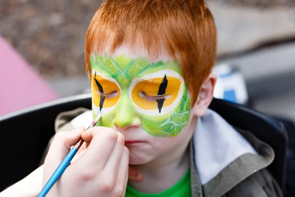 Child face painting process at redhead boy