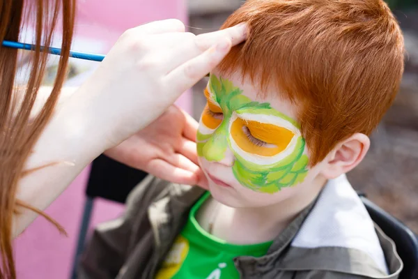 Child face painting process at redhead boy