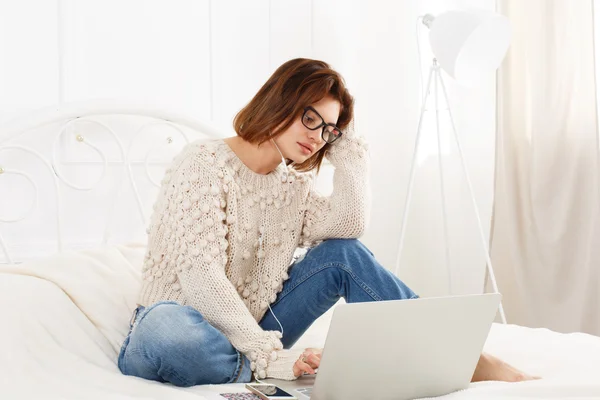 Young woman reads from laptop in bed, high key