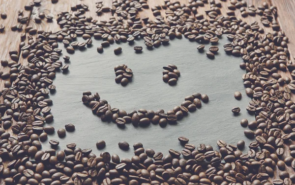 Smiley face from coffee beans at stone background