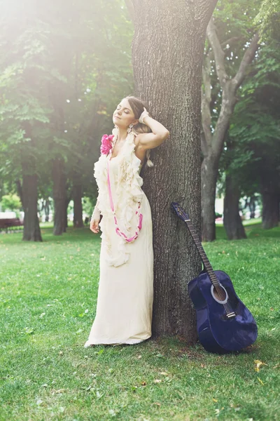 Portrait of beautiful boho girl near tree with blue guitar