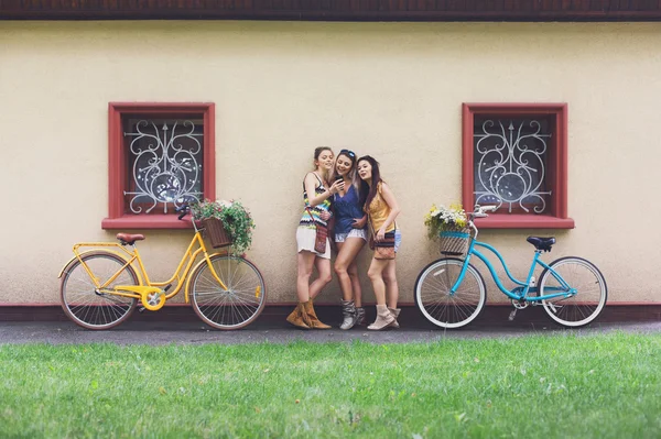 Happy boho chic girls pose with bicycles near house facade