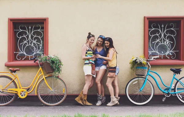 Happy boho chic girls pose with bicycles near house facade