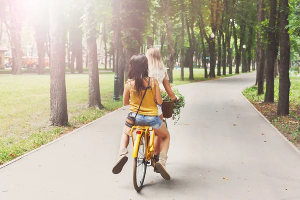 Happy boho chic girls ride together on bicycles in park