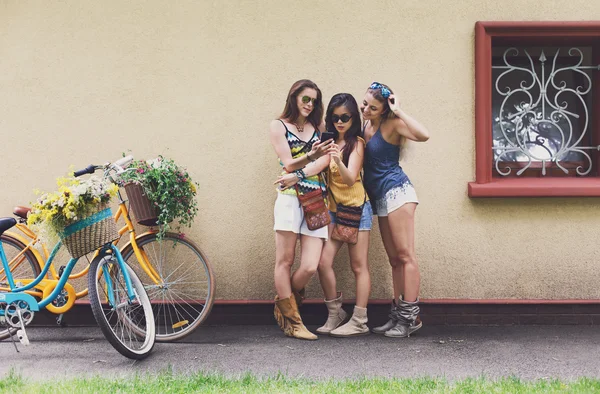 Happy boho chic girls pose with bicycles near house facade