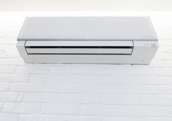 White air conditioner mounted on the brick painted wall