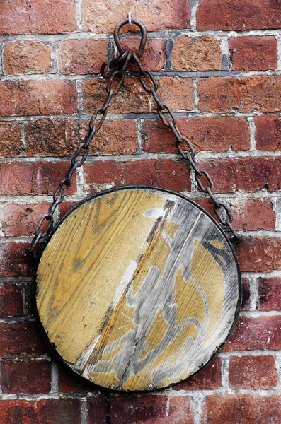 Round piece of blank wood hanging on a chain on red bricks wall. Copy space.