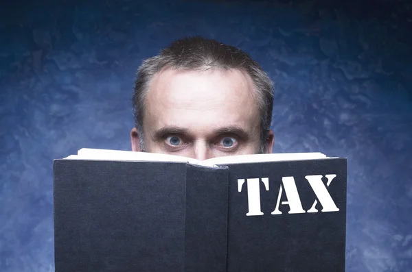 TAX written on the cover of the book, mature man being focused and hooked by book, reading open book,