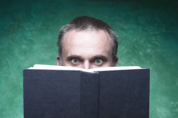 Mature man being focused and hooked by book, reading open book, surprised young man, amazing eyes looking blank cover, green background