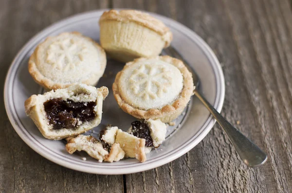 A sweet mince pie, a traditional rich festive food, on a plate with a fork on wooden background.