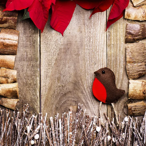 Frame arranged from poinsettia flowers, sticks, twigs, driftwood, coconut shell as a background. Handmade from felt bird robin. Craft.