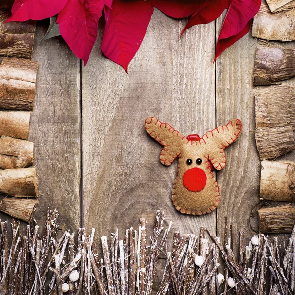 Frame arranged from poinsettia flowers, sticks, twigs, driftwood, coconut shell as a background. Handmade from felt Rudolph reindeer. Craft.