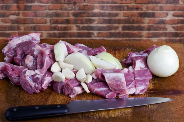 Raw cut meat, pork with cut onion and garlic on wooden cutting board. Red brick wall in background