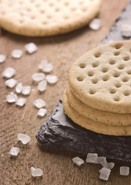 Crackers stack together on black stone, coarse sugar on wooden background.