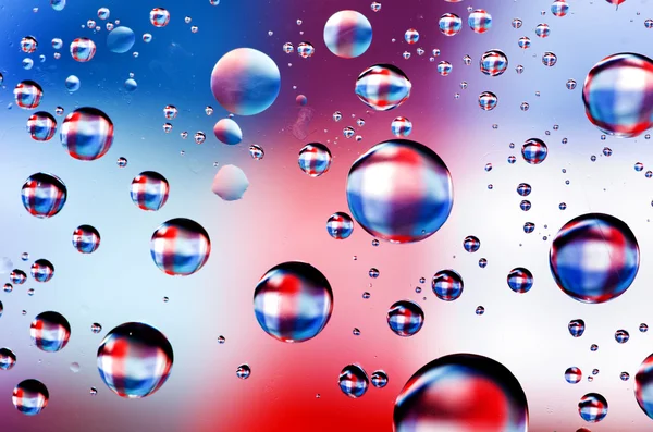 Close-up on water drops background on blue, red, white surface. Water droplets on glass with reflections in them.