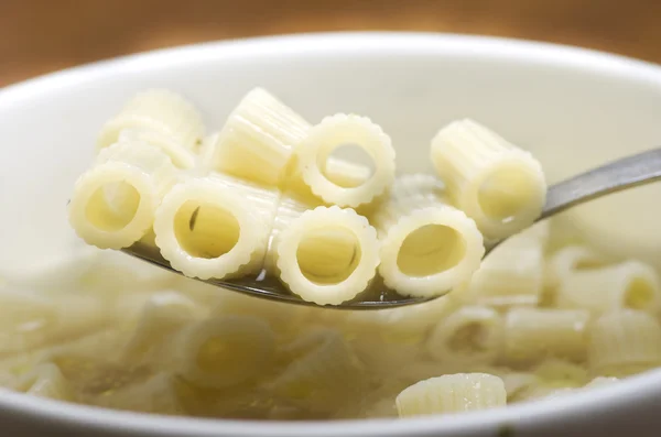 Close up of a bowl of macaroni soup. Spoon picking up macaroni, pasta.