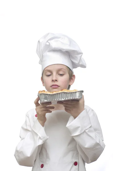 Young boy dressed as chef presenting fresh baked cake on white background.