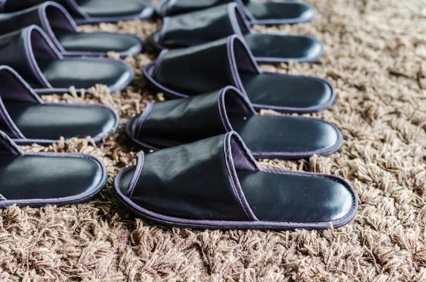 Row of black slippers on brown carpet