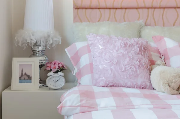 Pink bedroom with pink pillows on bed and white alarm clock on t