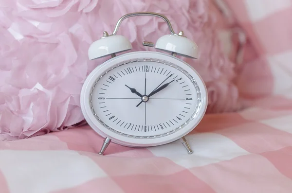 White modern alarm clock on pink bed