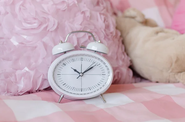 White modern alarm clock on pink bed