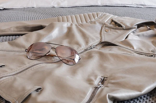 Sunglasses with brown jacket on bed
