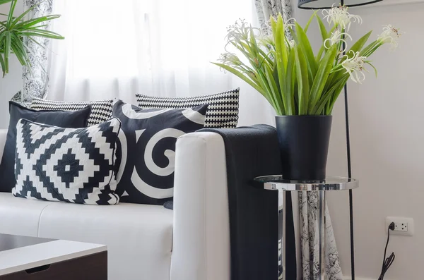 Black and white pillows on white sofa with vase of plant