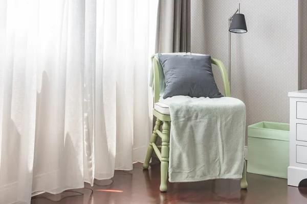 Green wooden chair with grey pillow and green blanket