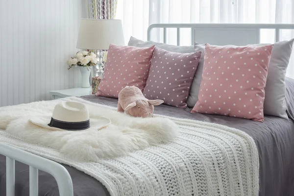 Pink pillows with pink doll on white wooden bed and classic hat