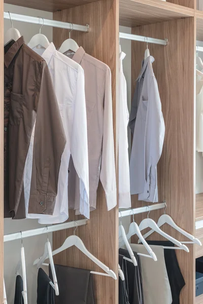 Shirts and pants hanging in wooden wardrobe