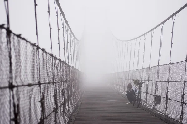 Girl sitting and playing smart phone on rope bridge and mystery fog ,Thailand