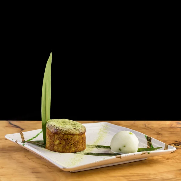 Cake filled with algae on a banana leaf with a scoop of ice cream. On a white plate and wooden table