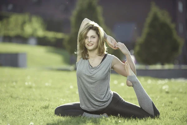 Young woman practicing yoga in the park on the green grass at sunset,smiling at the camera