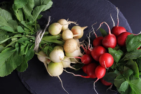 Radishes red and white on black background. Colorful vegetables on dark