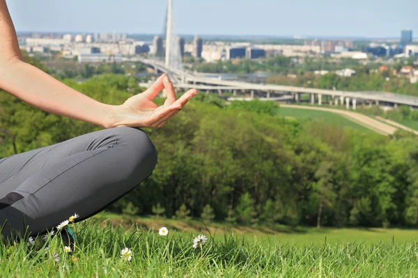 Yoga in the city : Woman meditating in yoga position in nature / park with city view close up.
