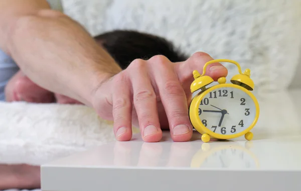 Man lying in bed turning off an alarm clock close up. Hate waking up early. Selective focus image