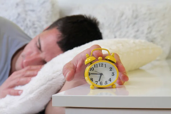 Man lying in bed turning off an alarm clock close up. Hate waking up early. Selective focus image