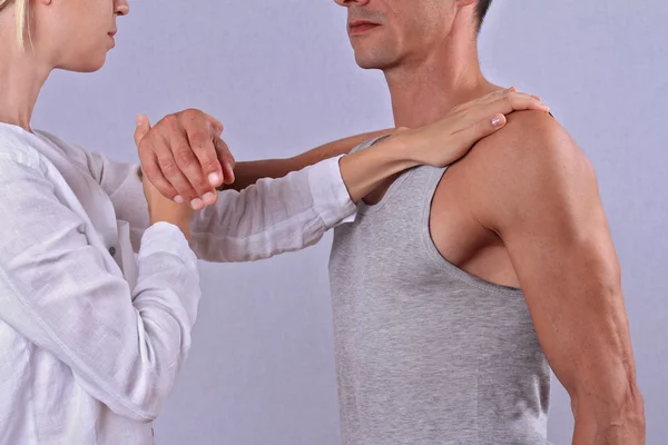 Therapist doing healing treatment on man\'s hand / shoulder. Alternative medicine, pain relief concept