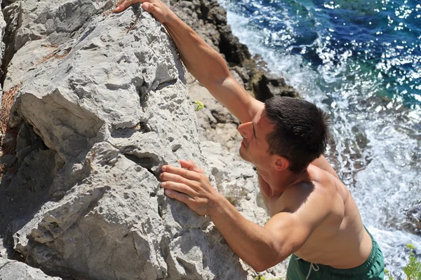 Attractive muscular Man climbing on mountain rocks against sea. Active summer vacation