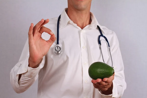 Doctor holding avocado and making all right sign. Health care concept, hypertension prevention