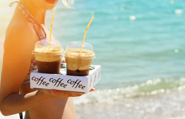Attractive female waiters holding two ice frappe coffee on the beach near sea. Young woman enjoyng during summer holiday, vacation  on tropical resort by ocean.