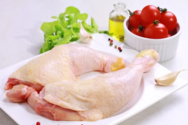 Raw chicken legs decorated with salad, olive oil and cherry tomatoes on white plate. Diet food, healthy lifestyle