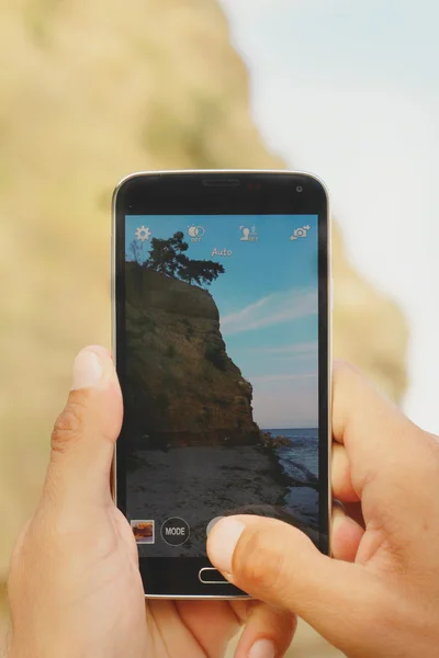 Close up on male hands taking photo of sea coast with mobile cell phone. Summer beach holiday vacation concept